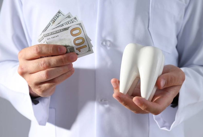 medico con soldi in una mano e miniatura di dente nell'altra
