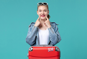 Giovane ragazza con valigia che indica sorriso