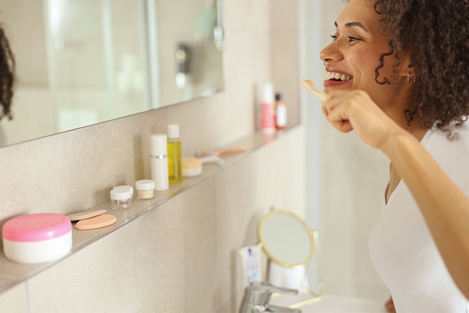 Nuove restrizioni sui cosmetici: impatti sulla salute orale Donna che si lava i denti guardandosi allo specchio