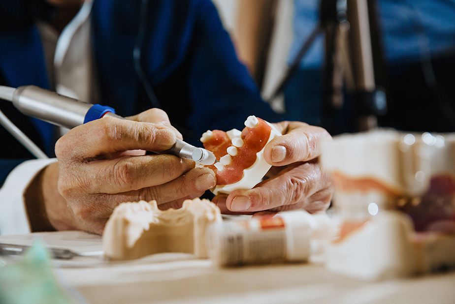 Professione sanitaria per gli odontotecnici: il dibattito resta aperto Primo piano di mani di odontotecnico che realizza una protesi