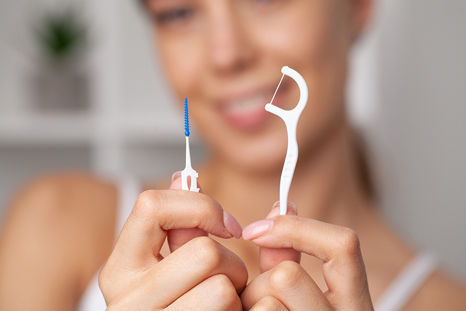 Più controlli dal dentista, ma l'igiene orale a casa resta incompleta Primo piano di mani di ragazza che tengono scovolino e filo interdentale